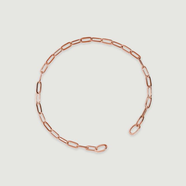 The rose gold bracelet lies diagonally with two rounded end loops visible.