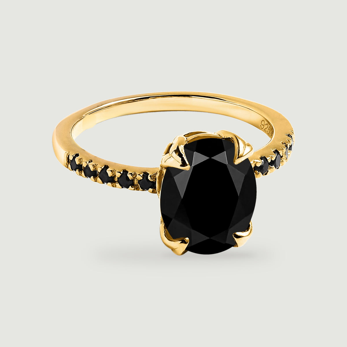 A yellow gold vermeil ring with an oval faceted black stone and black stones along its slender band rests on a light gray surface.