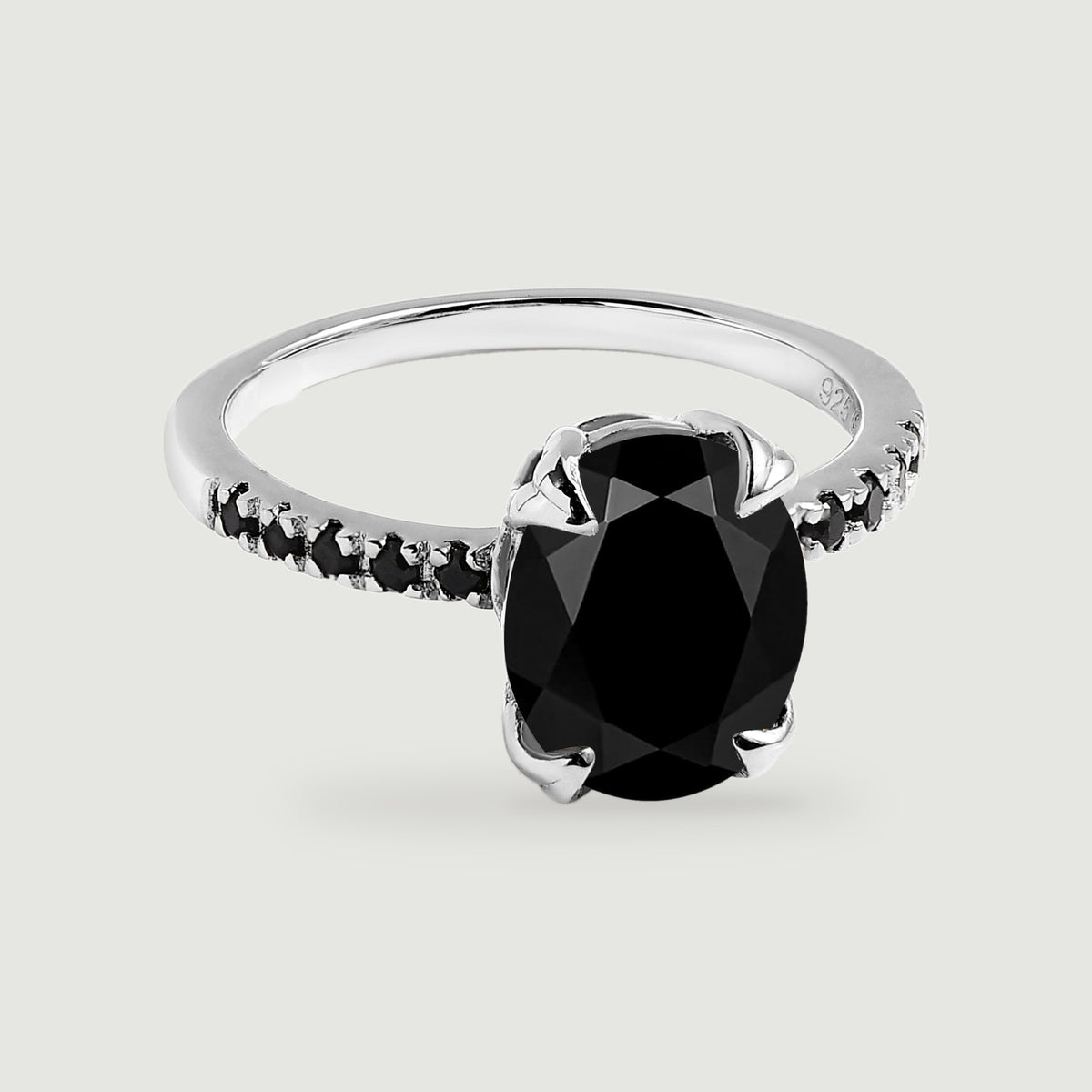 A sterling silver ring shows an oval black center stone, four polished prongs, and a row of small black stones on each shoulder.
