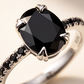 The faceted oval black stone fills the frame between silver prongs, with small black shoulder stones visible at the left.