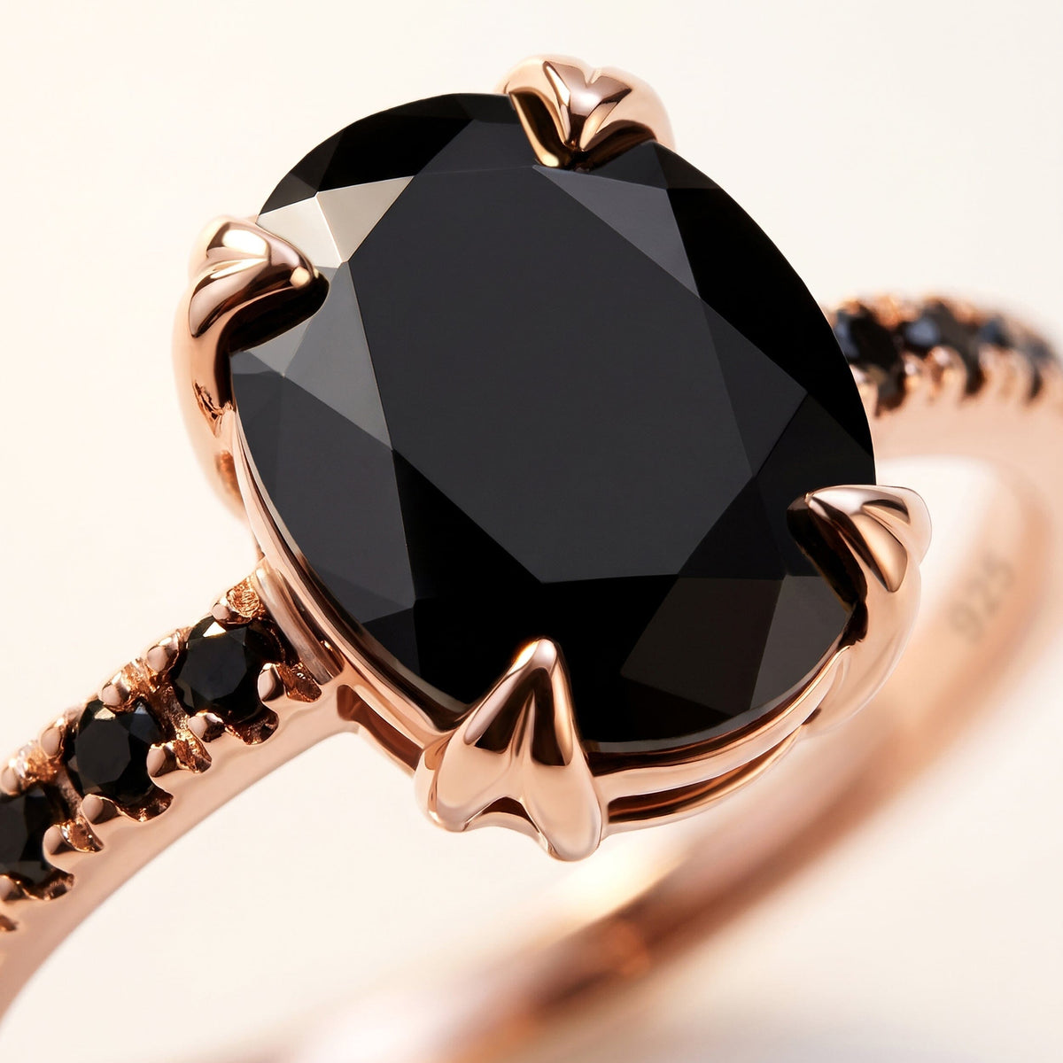 Polished rose gold prongs surround the large faceted black stone beside a narrow row of black accent stones.