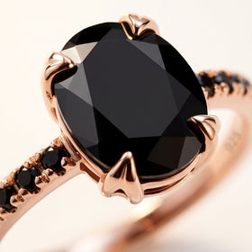 Polished rose gold prongs surround the large faceted black stone beside a narrow row of black accent stones.