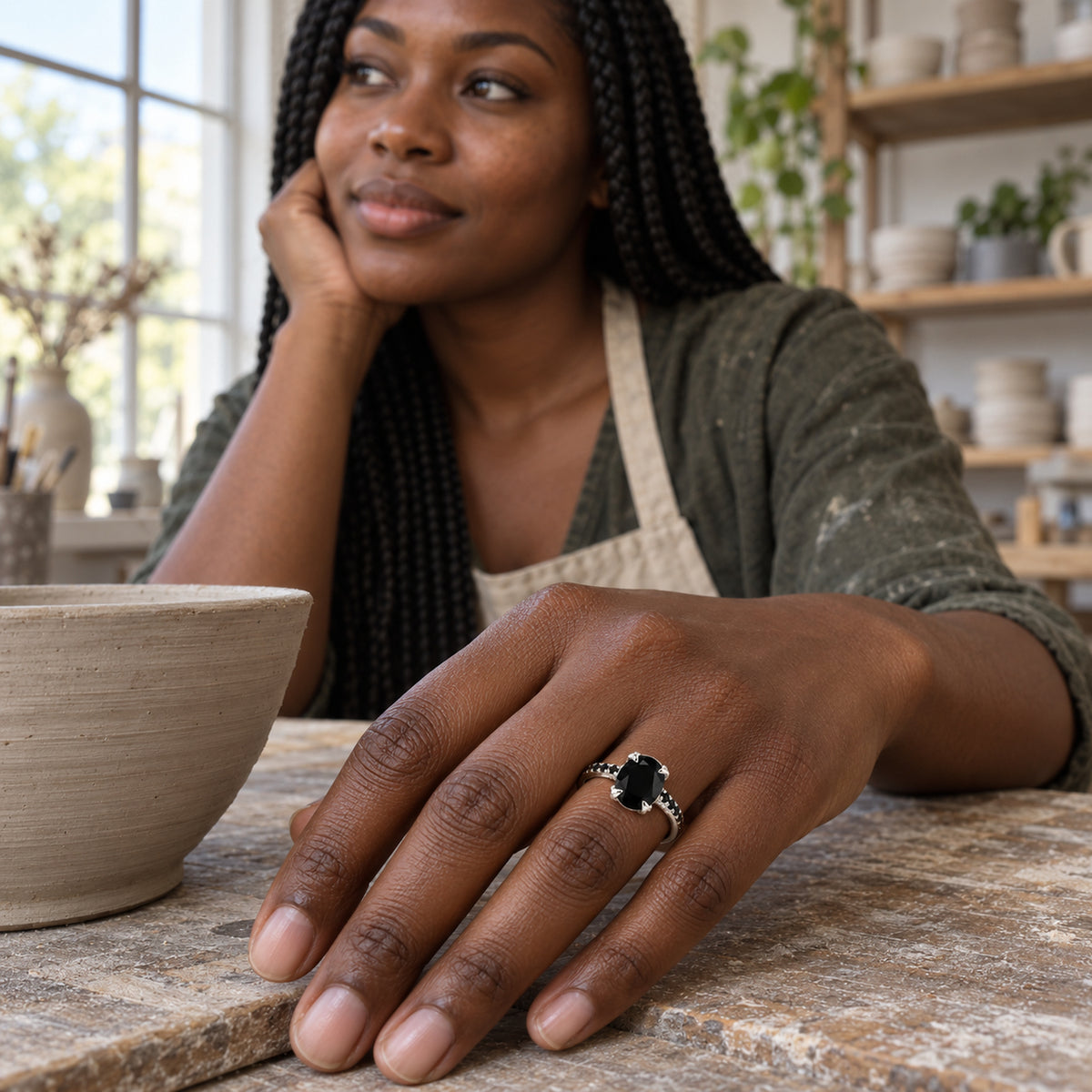 The silver ring sits on a woman's hand beside a clay bowl in a softly lit pottery studio.
