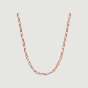 A rose gold necklace curves downward with polished rectangular links against a pale gray surface.