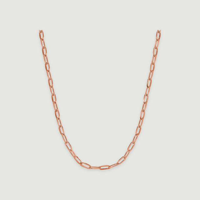 A rose gold necklace curves downward with polished rectangular links against a pale gray surface.