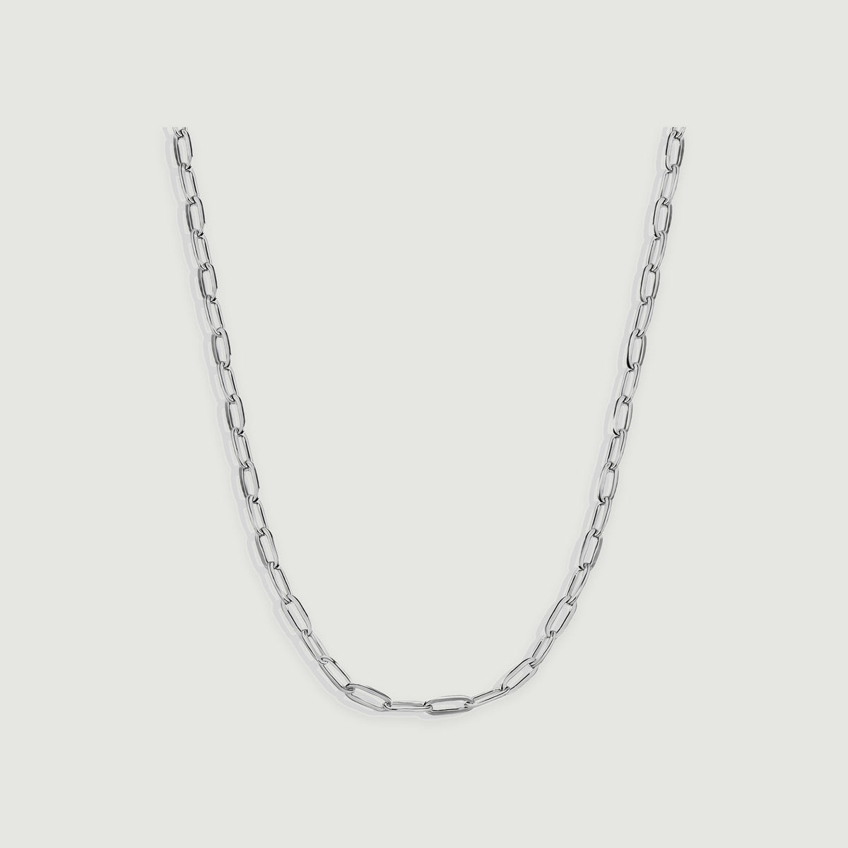 A silver chain necklace displays narrow reflective links arranged in a centered curve on light gray.