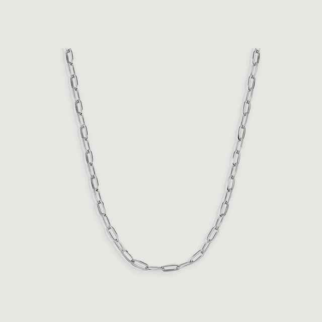 A silver chain necklace displays narrow reflective links arranged in a centered curve on light gray.