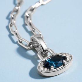 A close view shows the dark blue facets, clear side stones, and polished silver-tone pendant rim.