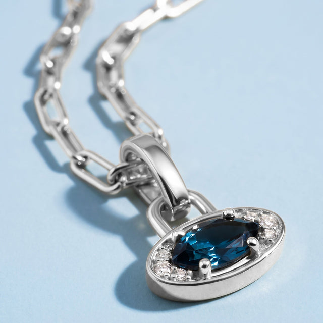 A close view shows the dark blue facets, clear side stones, and polished silver-tone pendant rim.