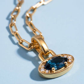 The blue gemstone sits between clear accent stones in a yellow gold-tone setting viewed at an angle.