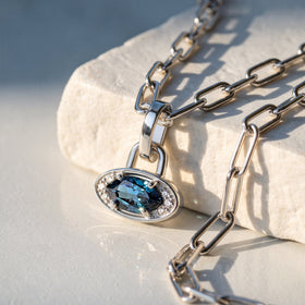 A silver-tone pendant and rectangular chain links rest across a pale stone block in sunlight.