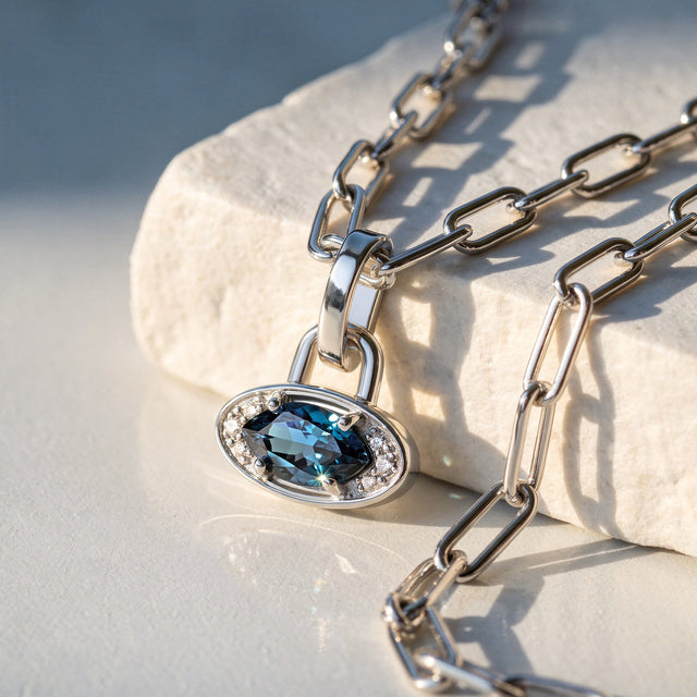 A silver-tone pendant and rectangular chain links rest across a pale stone block in sunlight.