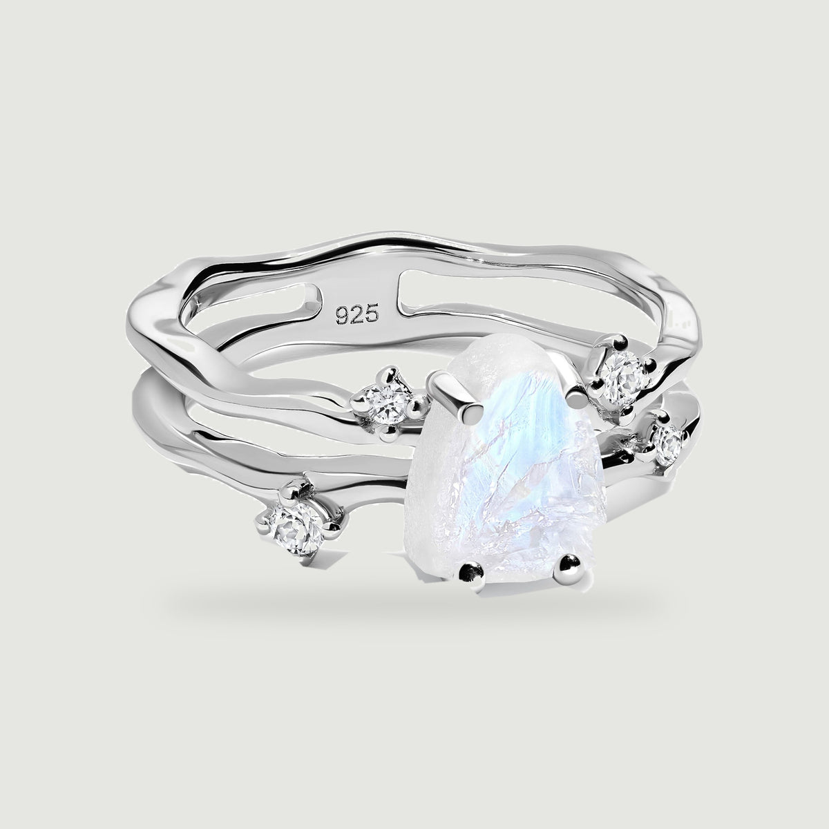 A silver ring with a rough white moonstone and four clear round stones rests on a light gray surface.