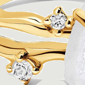 Two clear round stones sit beside the wavy yellow gold bands in a close view.