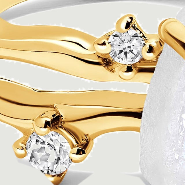 Two clear round stones sit beside the wavy yellow gold bands in a close view.