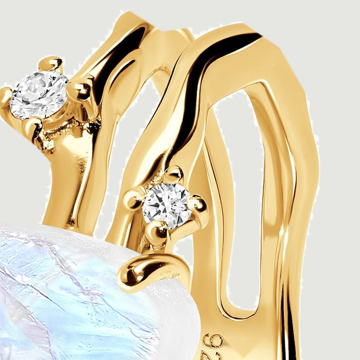 A close angled view shows two clear stones beside the yellow gold band and the pale moonstone edge.