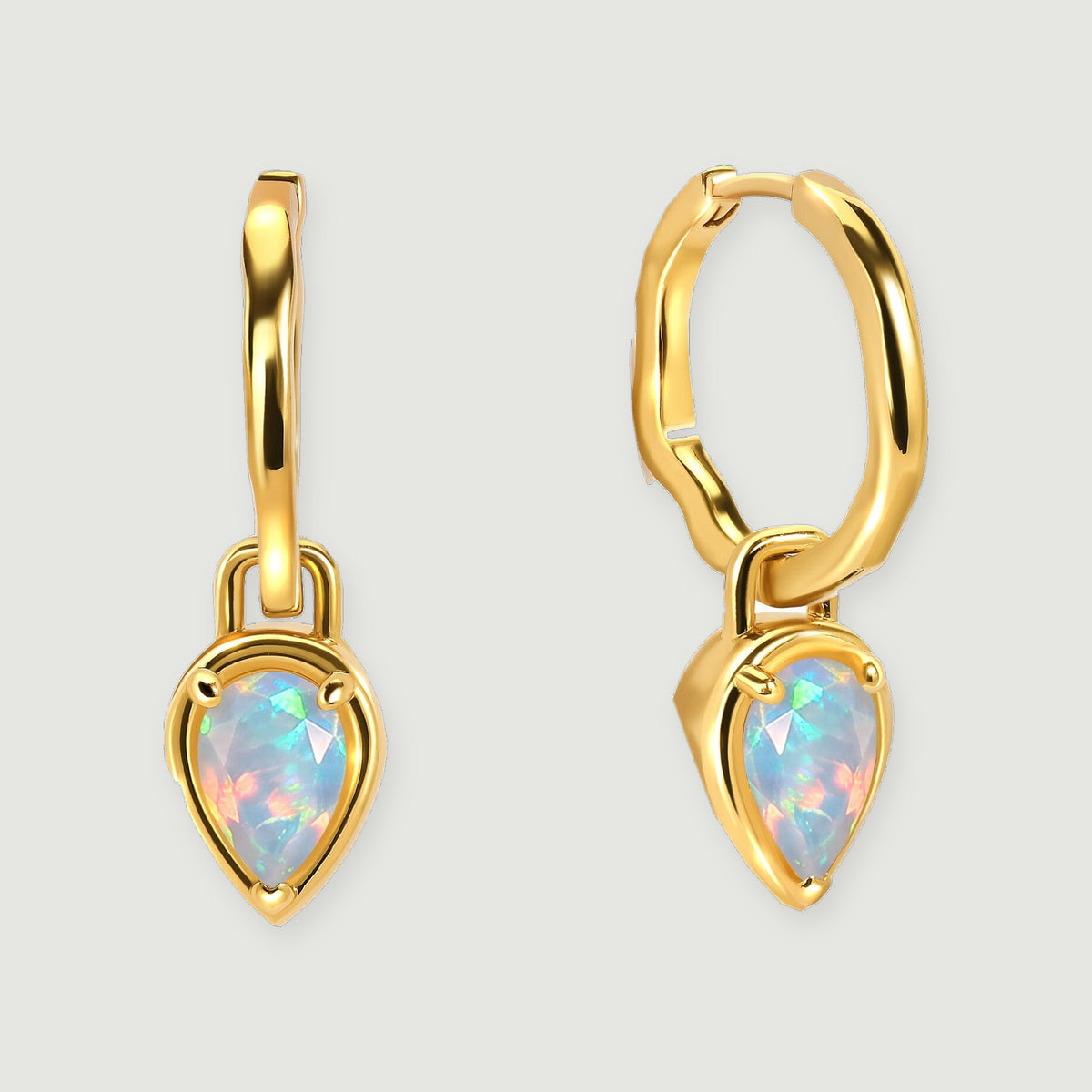 A pair of polished yellow gold hoops with pear-shaped opal drops rests against a pale gray background.