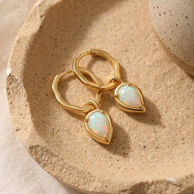 Yellow gold opal hoop earrings lie together on a textured beige ceramic tray.