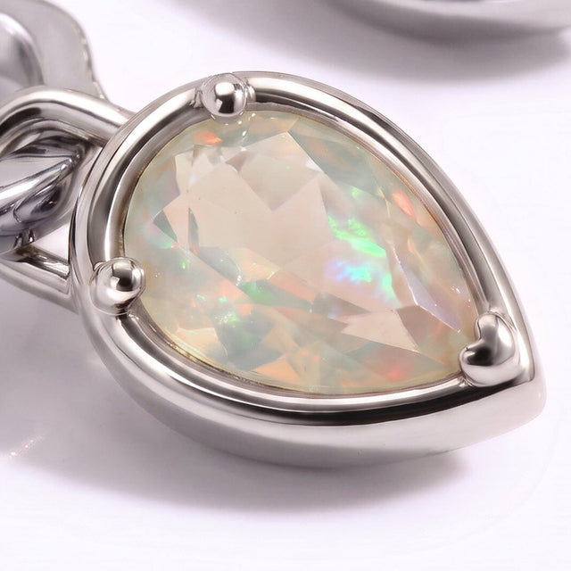 A faceted opal reflects green and peach colors inside a silver-tone three-prong setting.