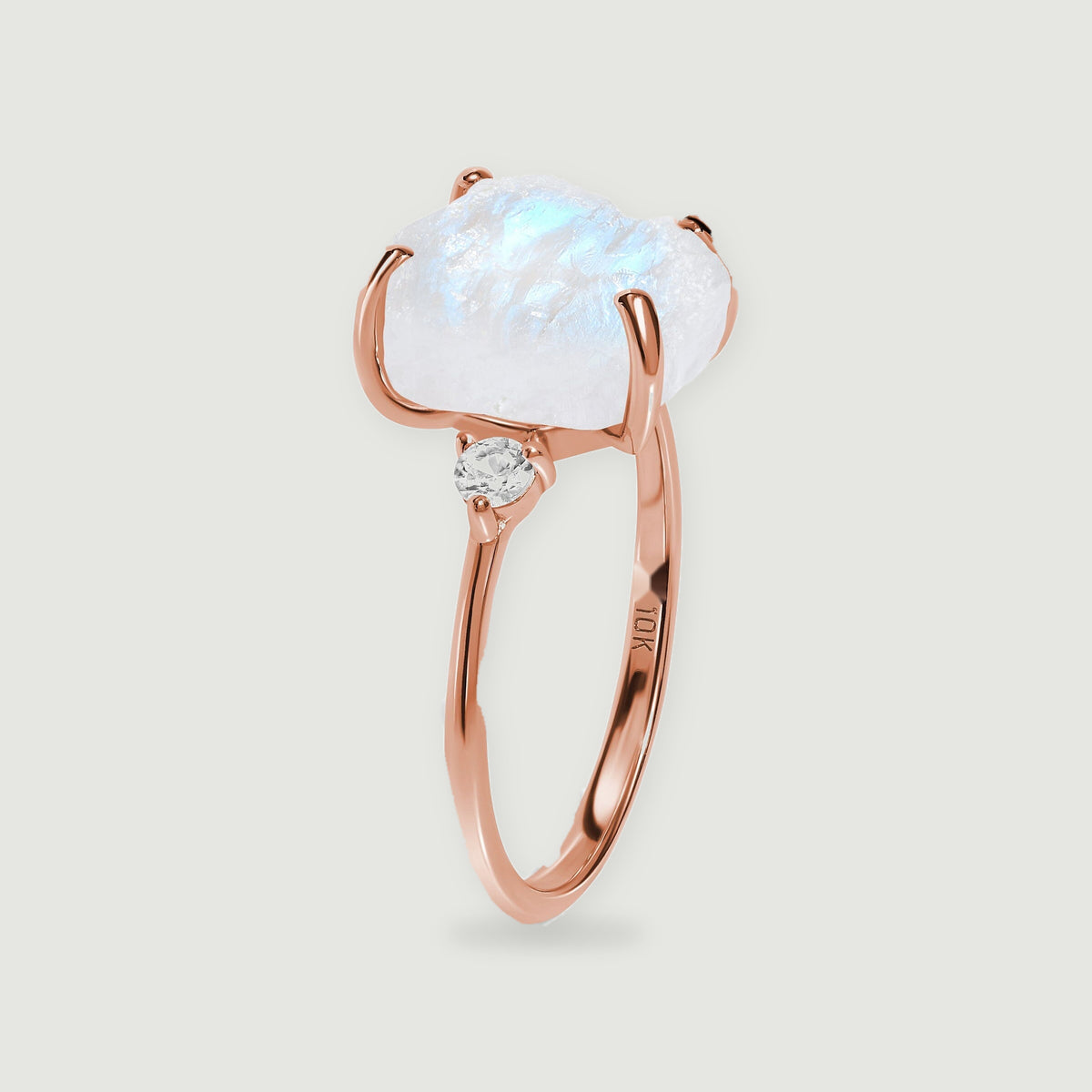 A side view shows the rose gold band, a round accent stone, and the moonstone held above the ring.