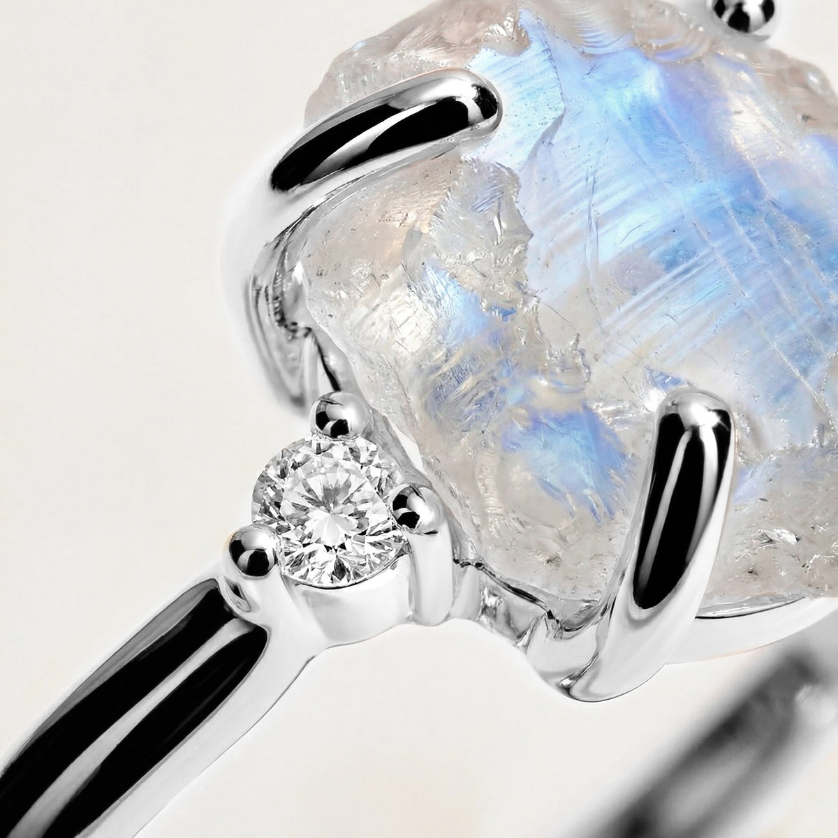 A close-up reveals blue flashes in the rough moonstone beside a round clear stone and polished white gold prongs.