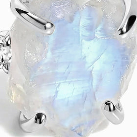 The front of the rough moonstone shows layered blue-white reflections between the lower white gold prongs.
