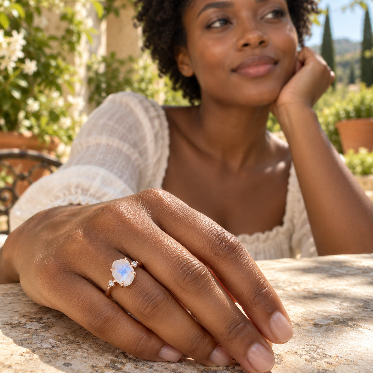 A woman rests her hand on a garden terrace table while wearing the rose gold moonstone ring.