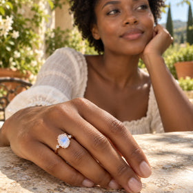 A woman rests her hand on a garden terrace table while wearing the rose gold moonstone ring.