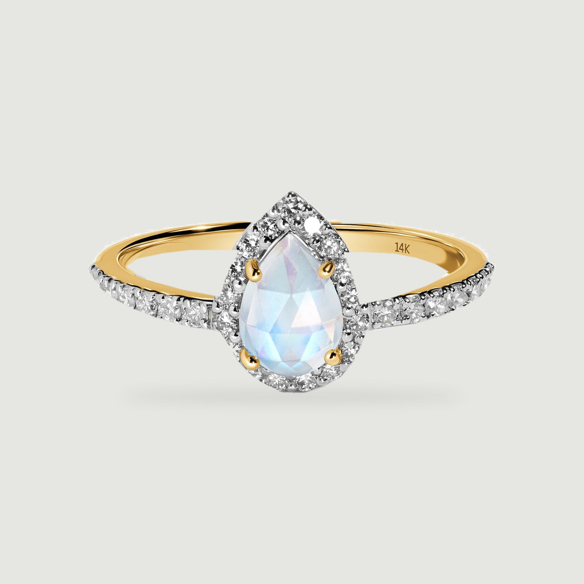 A yellow gold ring displays a pear-shaped moonstone framed by diamonds on a light grey surface.