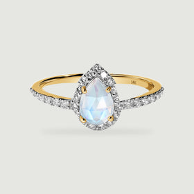 A yellow gold ring displays a pear-shaped moonstone framed by diamonds on a light grey surface.