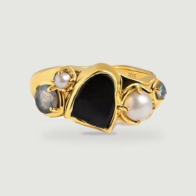 A yellow gold vermeil ring with a black center stone, two white pearls, and two blue-gray side stones on a light gray background.