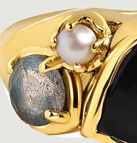 A blue-gray side stone and small white pearl sit in gold prongs beside the black center stone.