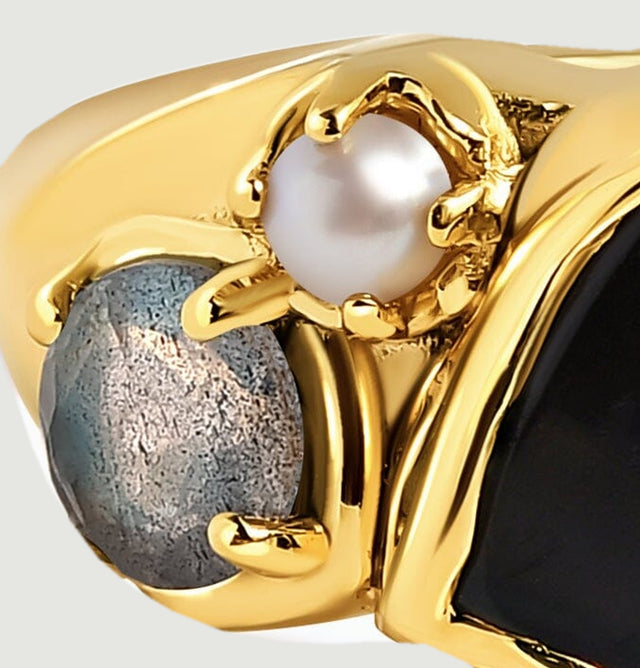 A blue-gray side stone and small white pearl sit in gold prongs beside the black center stone.