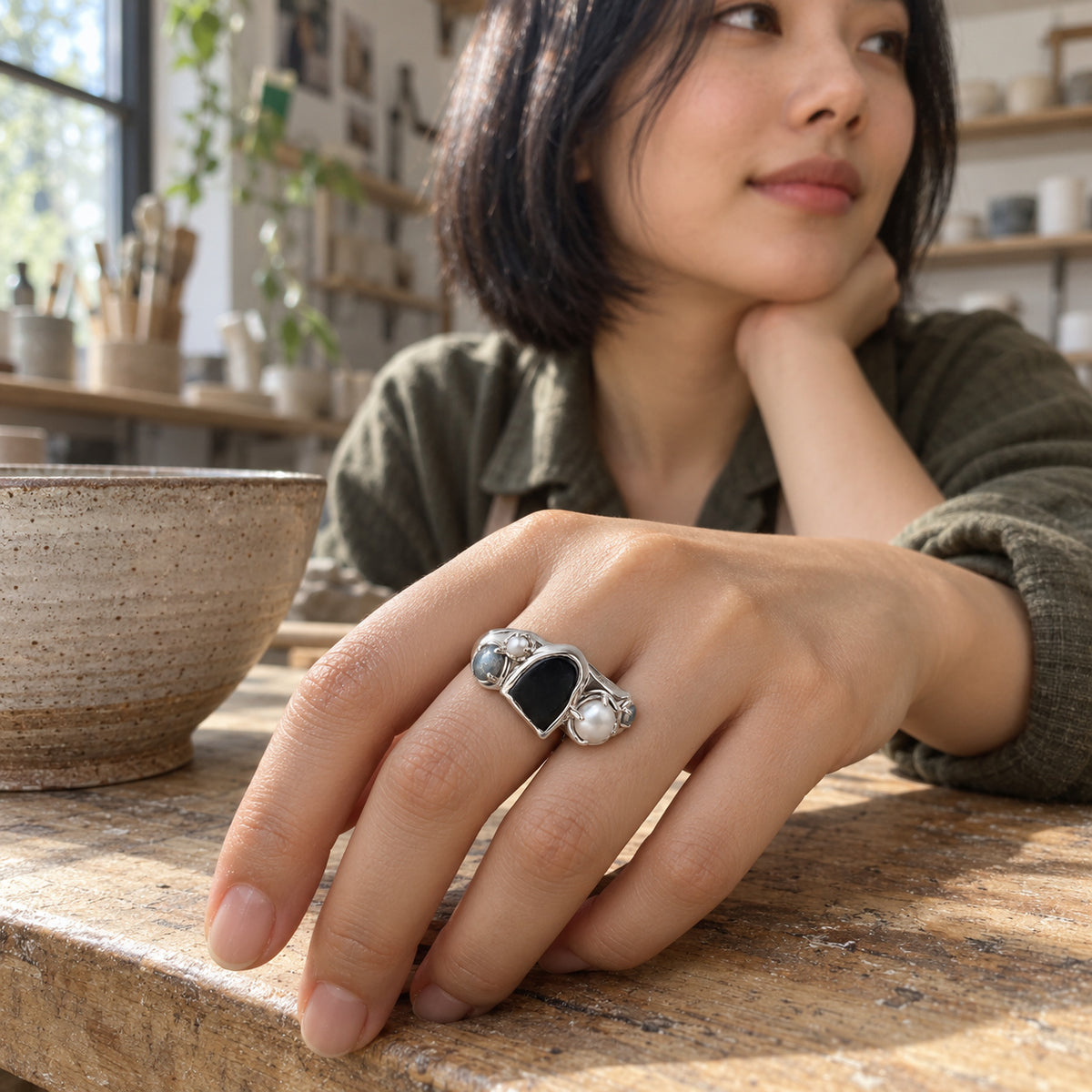 A woman in an olive shirt wears the silver ring with her hand resting on a wooden table beside a pottery bowl.