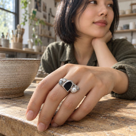 A woman in an olive shirt wears the silver ring with her hand resting on a wooden table beside a pottery bowl.