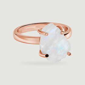 A raw white moonstone with blue flashes is held by four rounded prongs on a polished rose gold band.