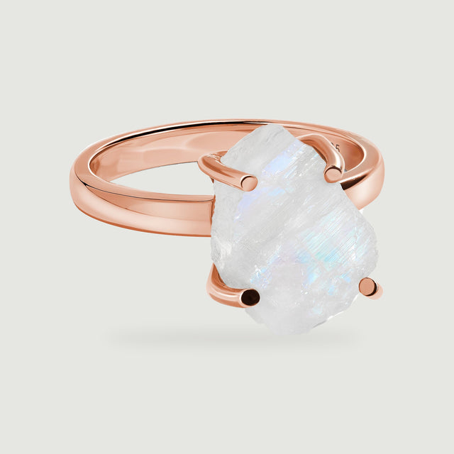 A raw white moonstone with blue flashes is held by four rounded prongs on a polished rose gold band.