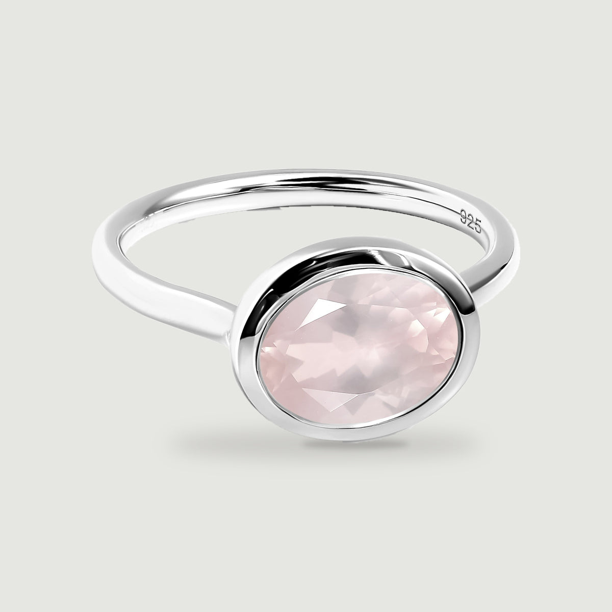 An oval rose quartz is framed by a polished silver bezel above a slender circular band.