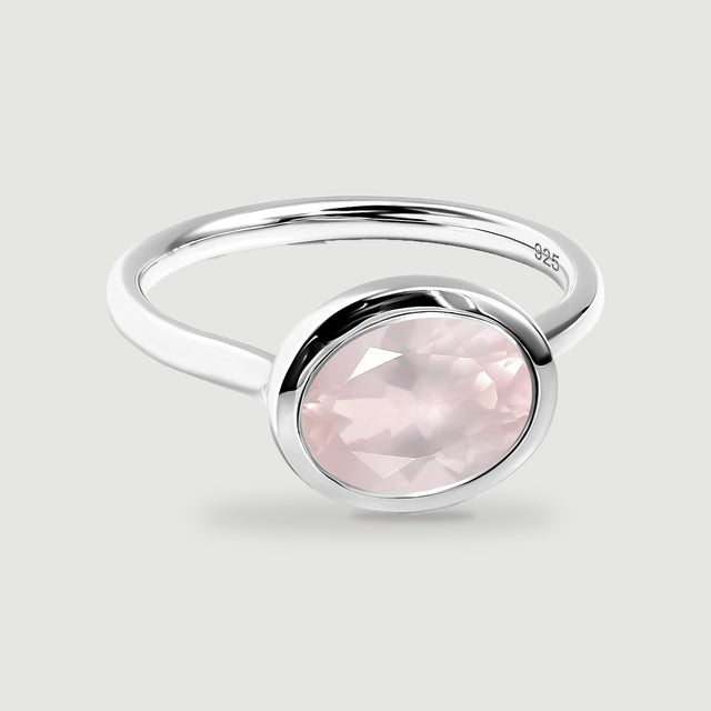 An oval rose quartz is framed by a polished silver bezel above a slender circular band.