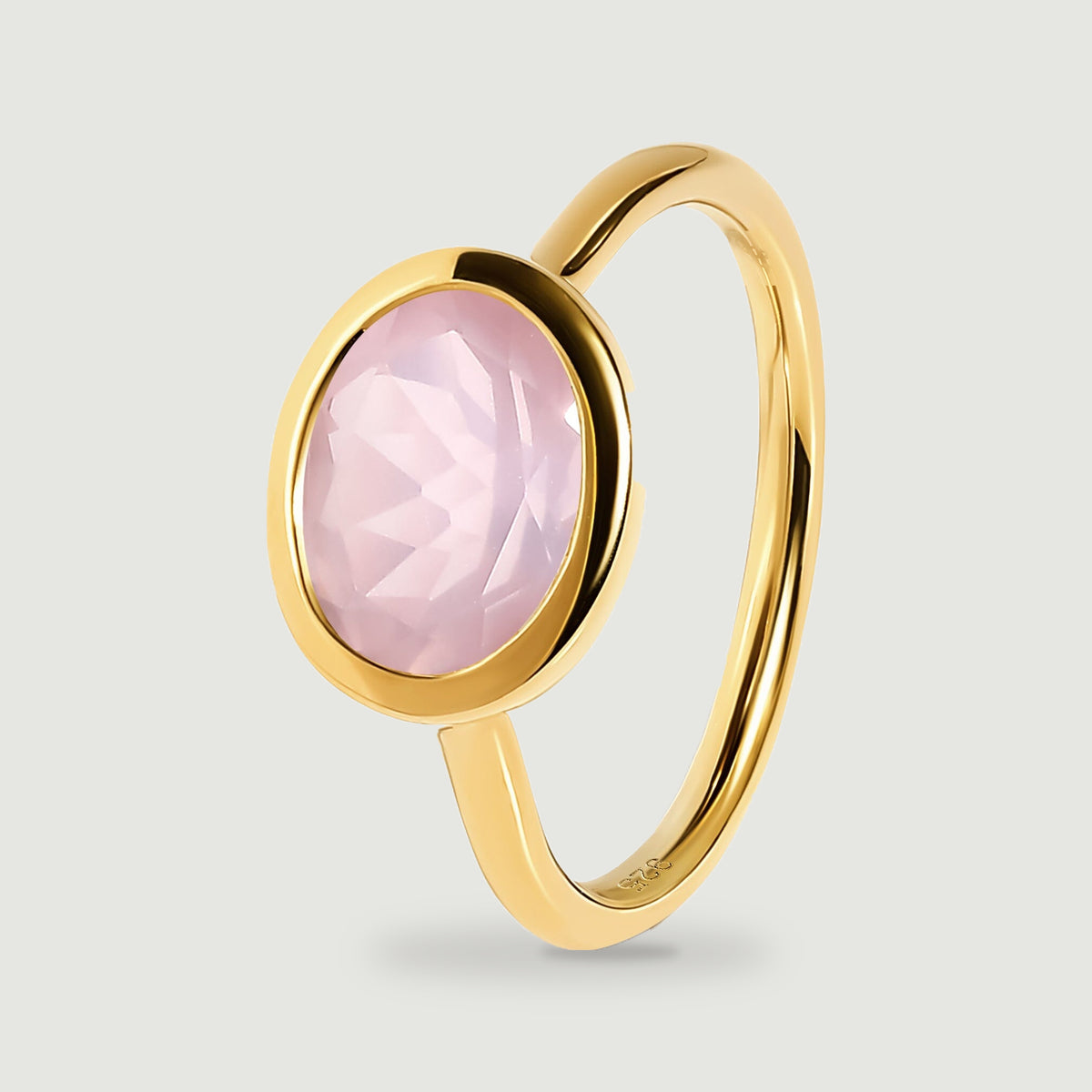 An angled yellow gold band surrounds an oval pink gemstone with visible geometric facets.
