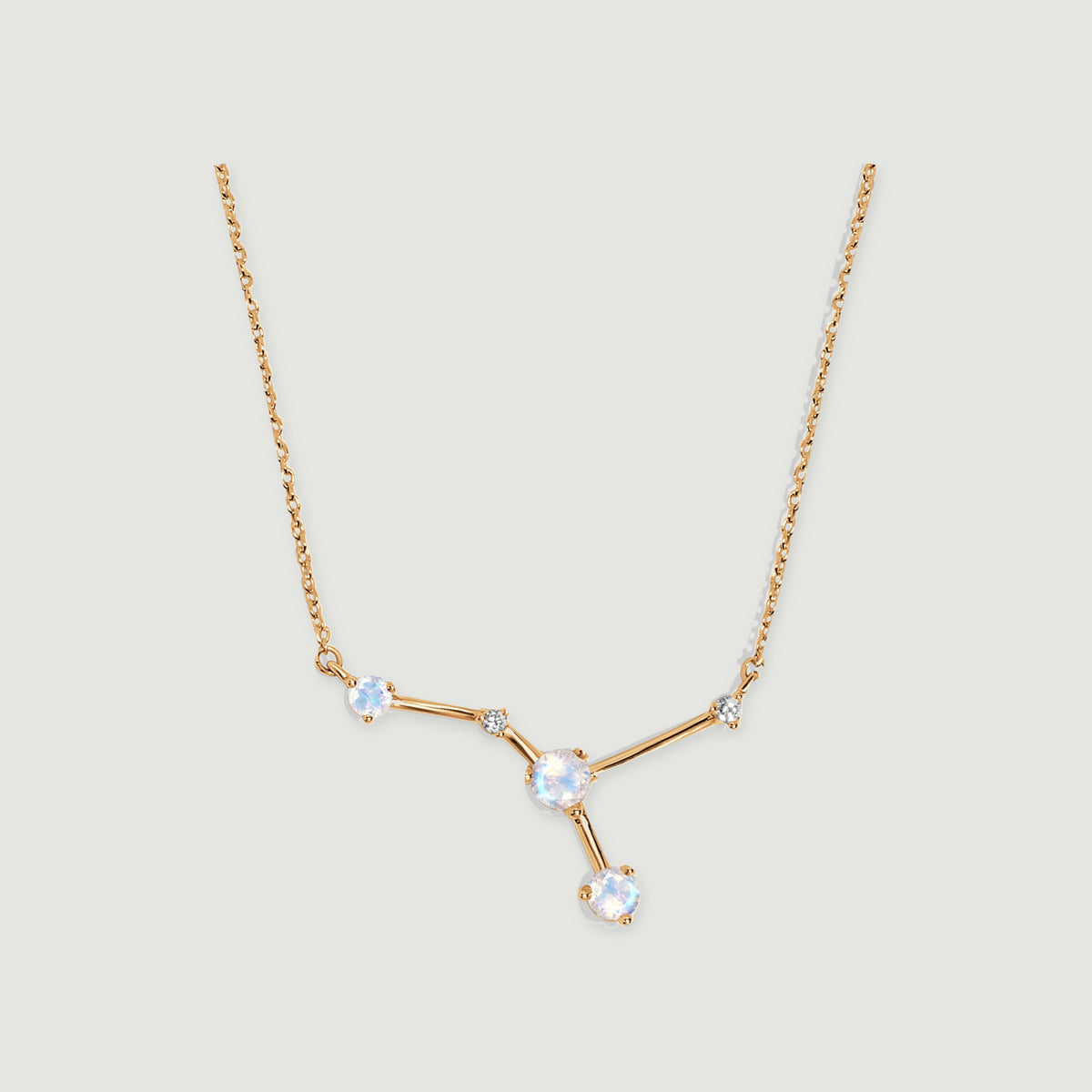 A yellow gold necklace with a branching moonstone pendant rests against a light grey background with a soft shadow.