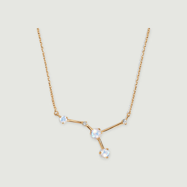 A yellow gold necklace with a branching moonstone pendant rests against a light grey background with a soft shadow.