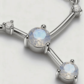 A close view shows the blue sheen of a round moonstone, silver prongs and small clear stones along polished connecting bars.
