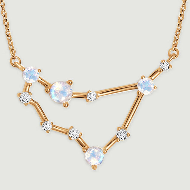 Four pale round stones sit along the yellow gold bars of a geometric pendant.