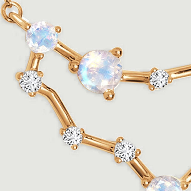 Two iridescent round stones and several clear accents are held by yellow gold prongs.