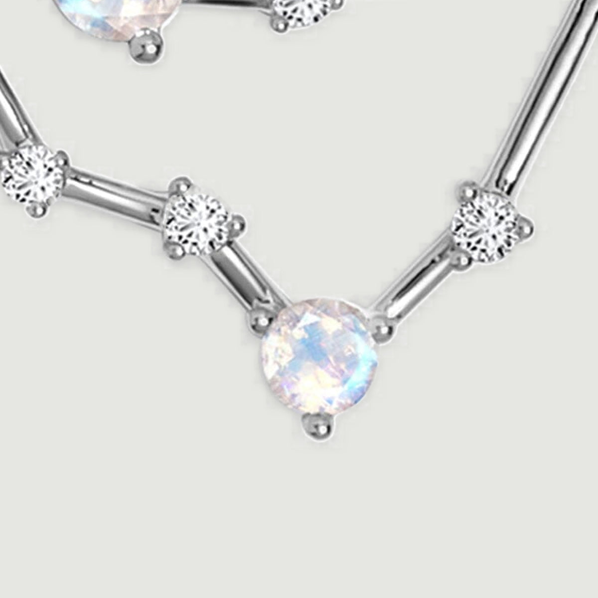 A round pale stone forms the lower point of the silver pendant beside clear accent stones.