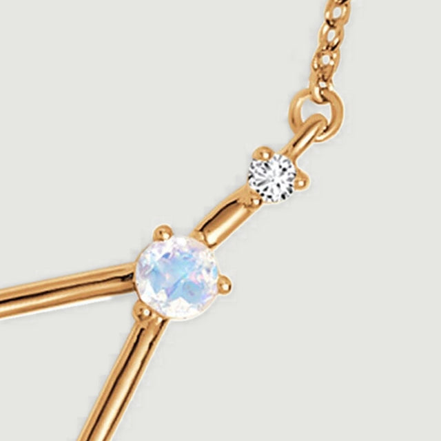 A yellow gold chain attachment leads to a small clear stone and a pale round stone.