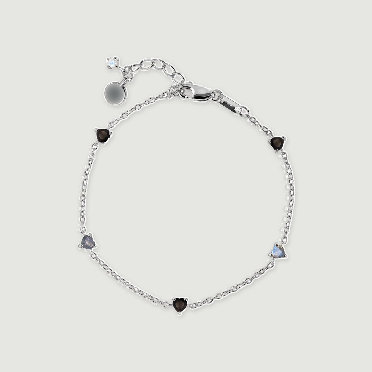 A sterling silver chain bracelet forms an oval with alternating black and blue gray heart shaped stones.