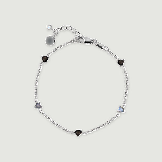 A sterling silver chain bracelet forms an oval with alternating black and blue gray heart shaped stones.