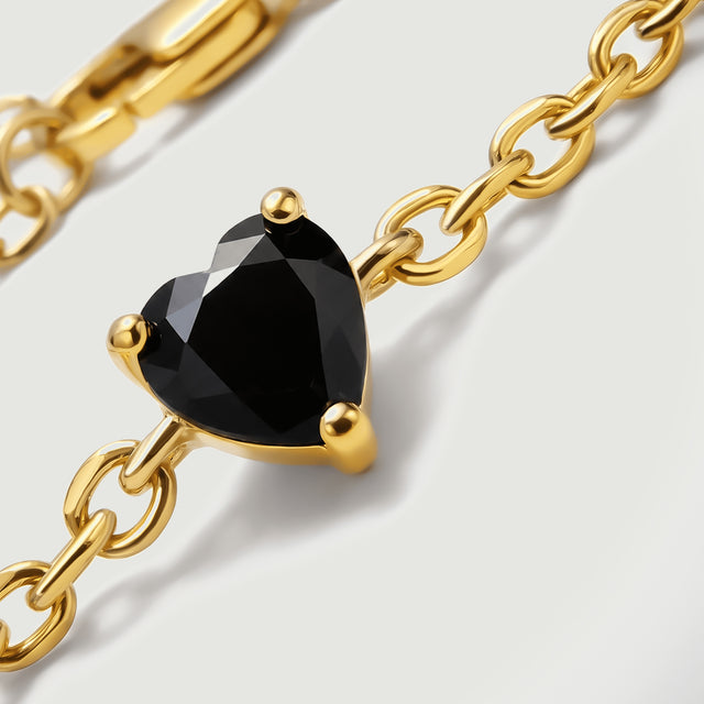 A glossy black heart shaped stone is held by three yellow gold prongs along a fine chain.